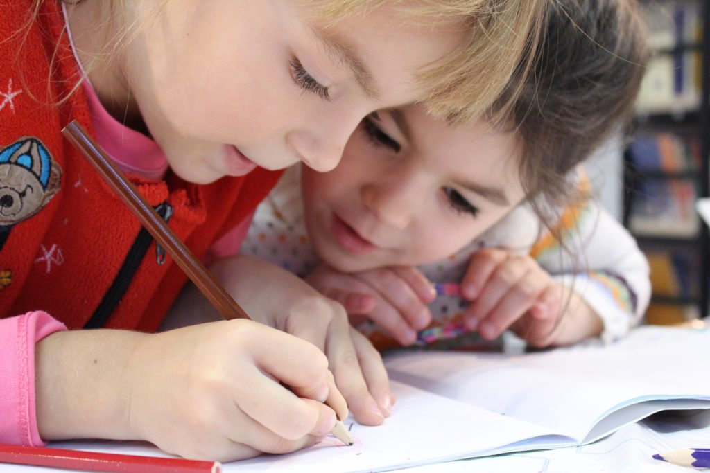 Young girls leaning on desk while writing in a notebook with a colored pencil