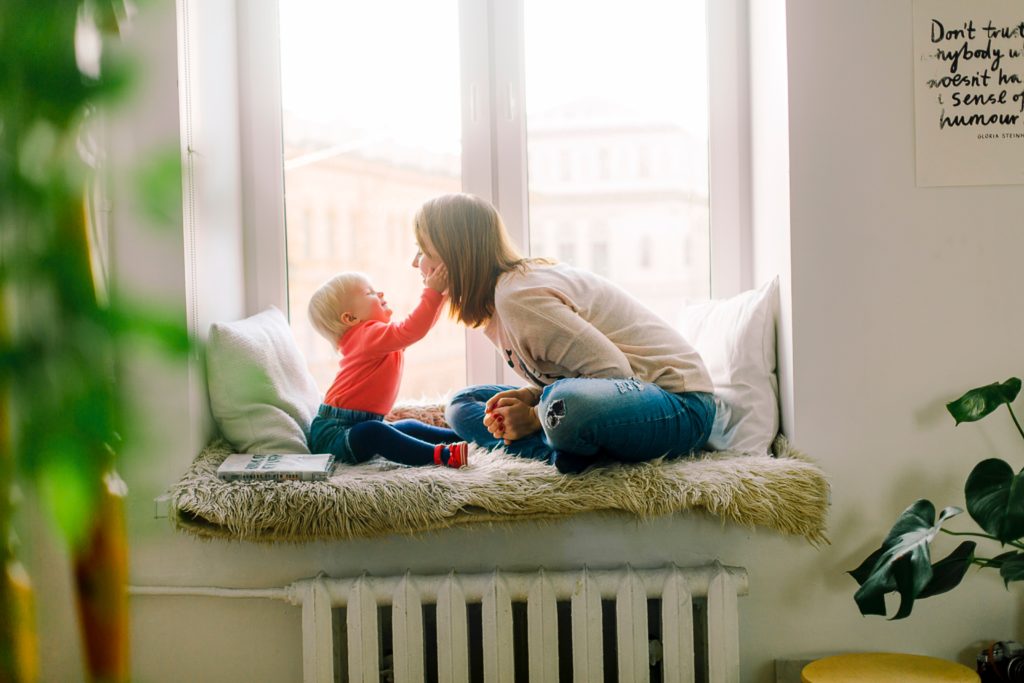 baby touching a woman's face while both sit on a window seat