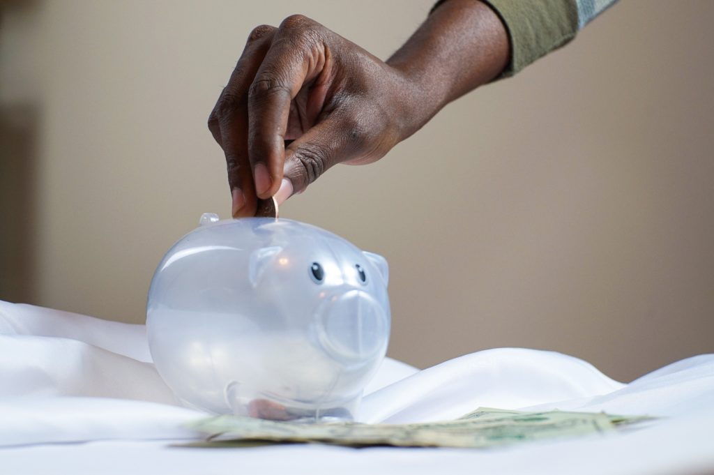 Hand putting coin into white plastic piggy bank